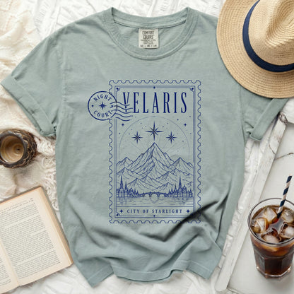 Light blue t-shirt with a blue postage stamp graphic of Velaris, City of Starlight.