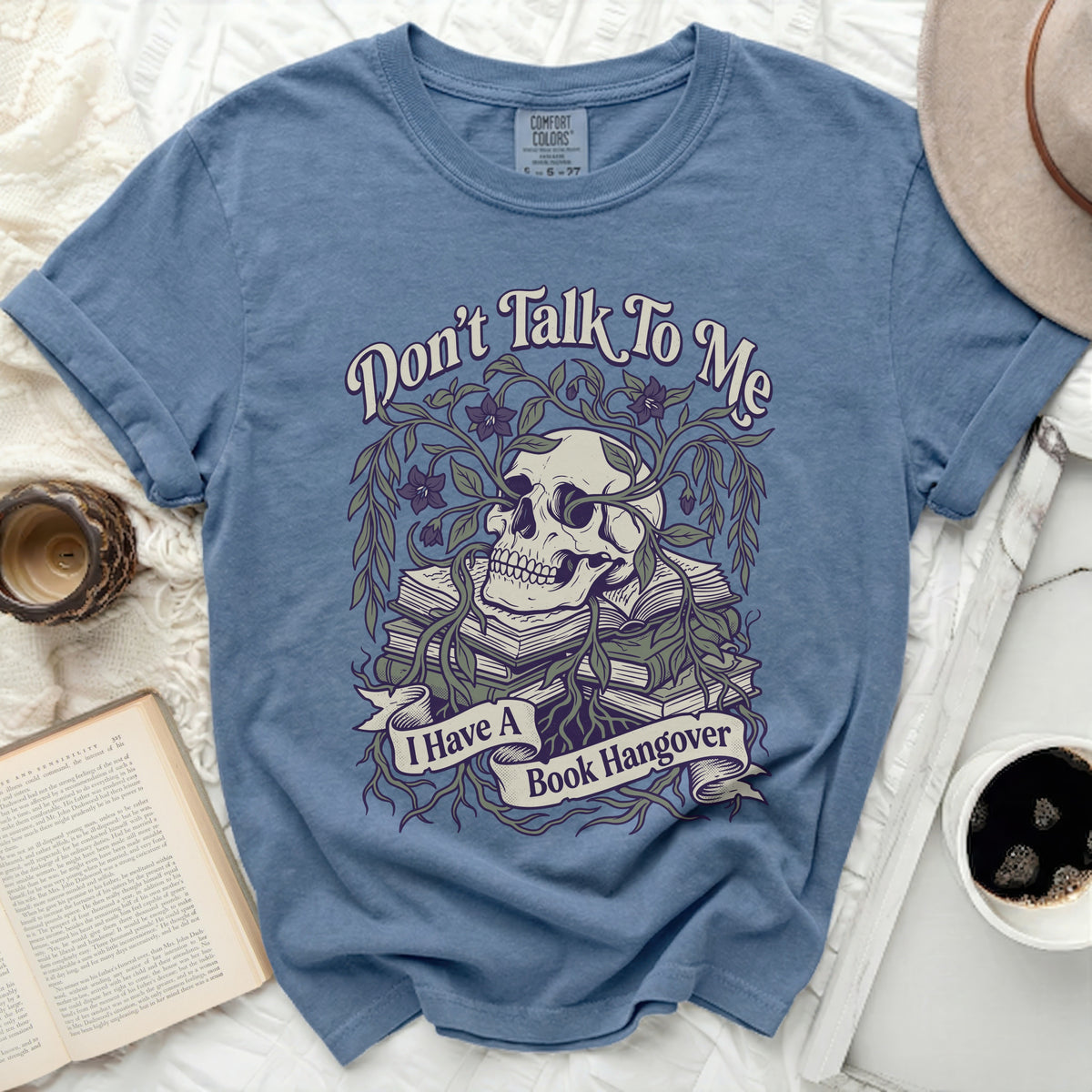 Blue t-shirt with skull, books, vines, and text "Don't Talk To Me I Have A Book Hangover".
