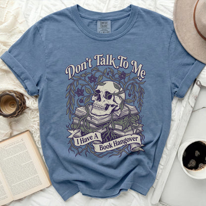 Blue t-shirt with skull, books, vines, and text "Don't Talk To Me I Have A Book Hangover".