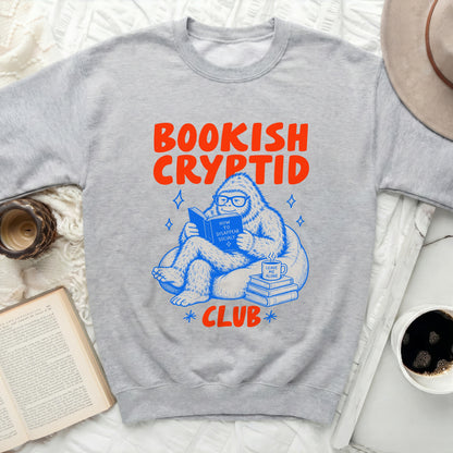 Grey sweatshirt with "Bookish Cryptid Club" graphic and reading Bigfoot.