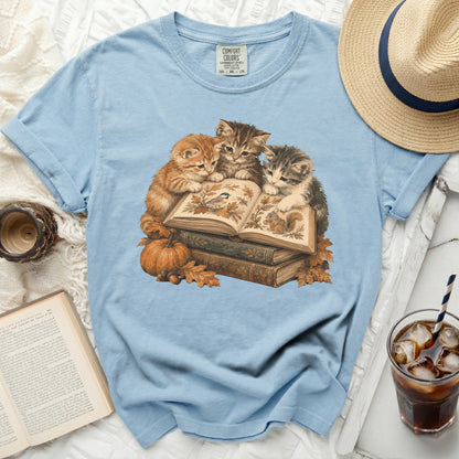 Light blue t-shirt with three kittens reading a book and autumn leaves.