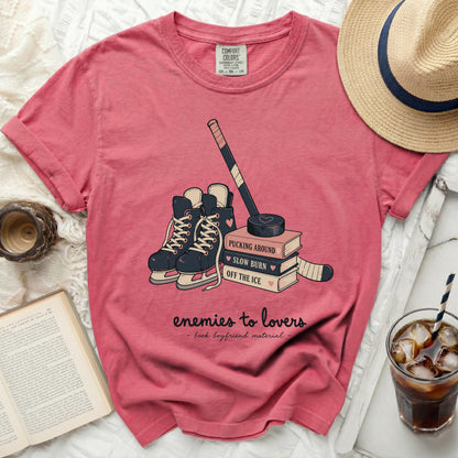 Pink t-shirt with hockey skates, puck, and books with "enemies to lovers" text.