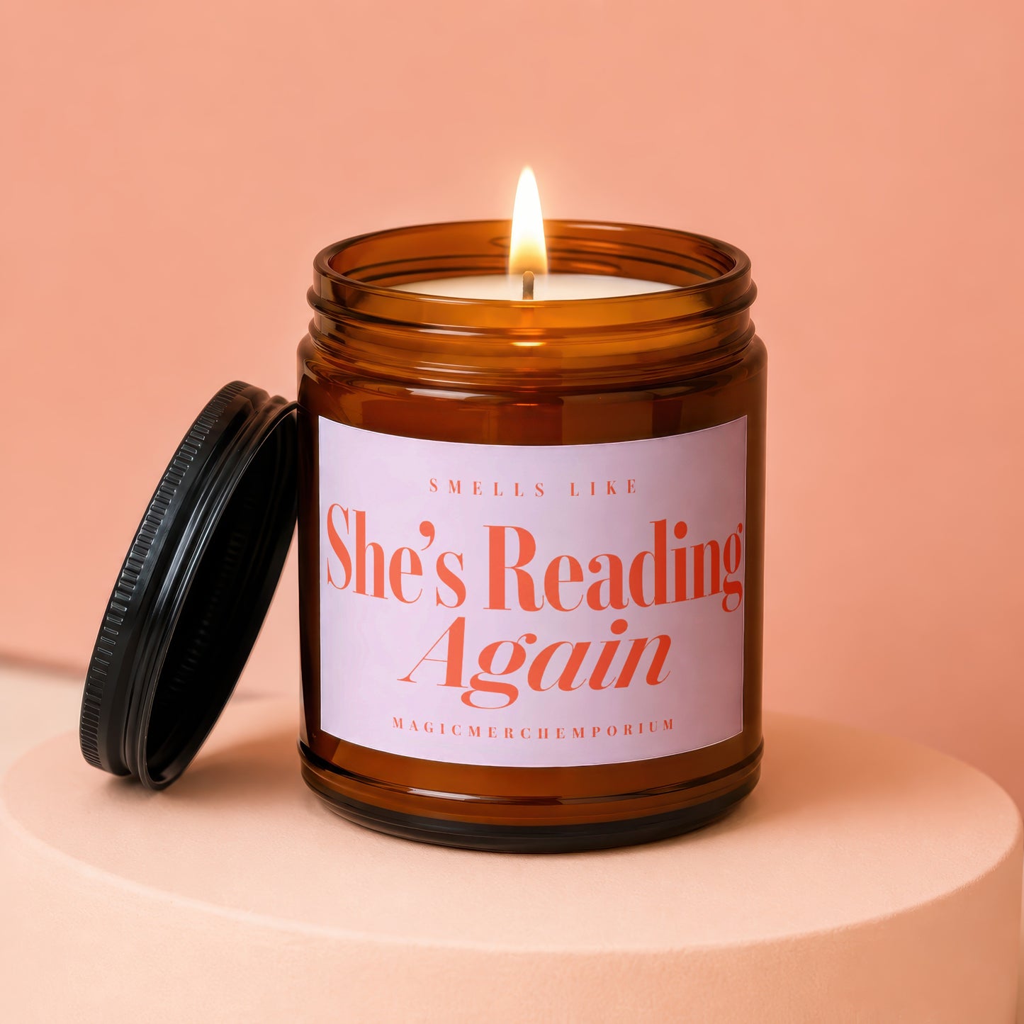 Amber jar candle with lit wick reads "Smells Like She's Reading Again".