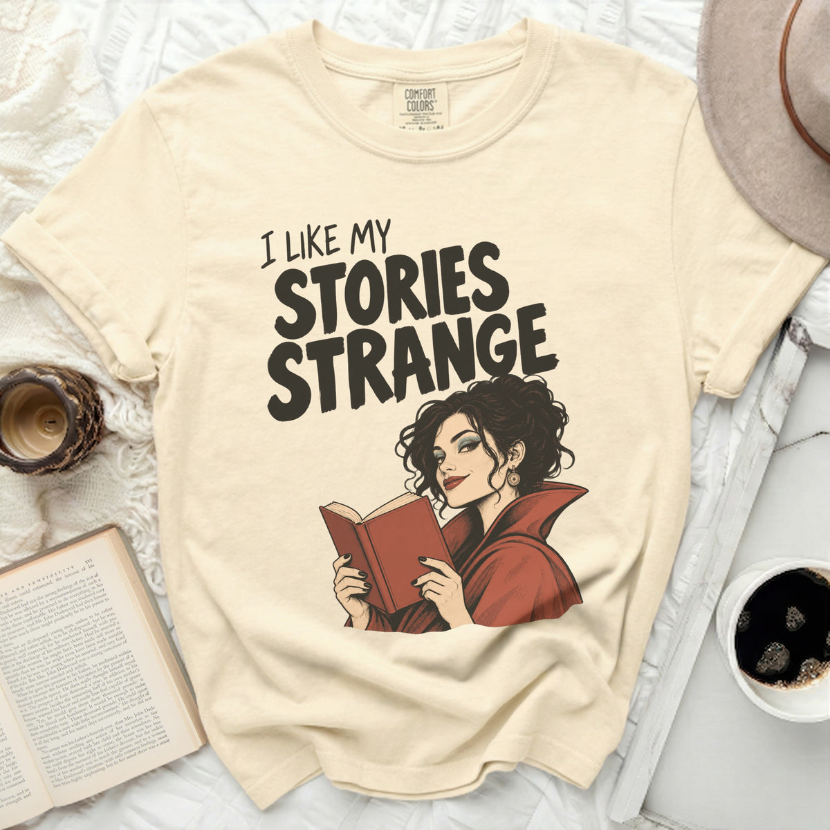Light cream t-shirt with "I Like My Stories Strange" text and a woman reading.