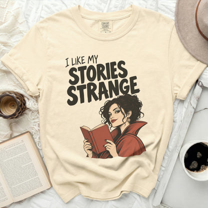 Light cream t-shirt with "I Like My Stories Strange" text and a woman reading.