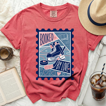 T-shirt with a stamp design featuring hockey skates, puck, stick, book, and "Booked By Love" text.