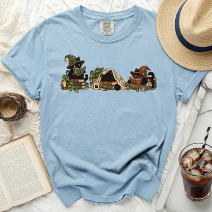 Light blue t-shirt with a graphic of three black cats reading books and sleeping.