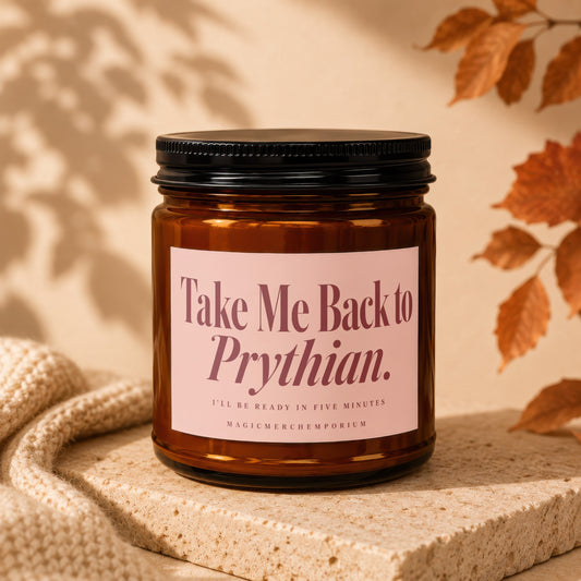 An amber glass jar candle with a black lid and pink label reading Take Me Back to Prythian.