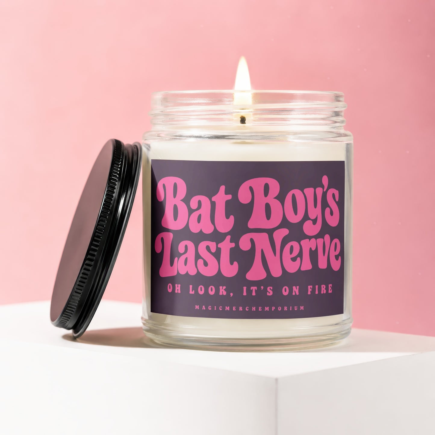 Candle with lit wick, glass jar, black lid, and label reading "Bat Boy's Last Nerve Oh Look, It's On Fire".