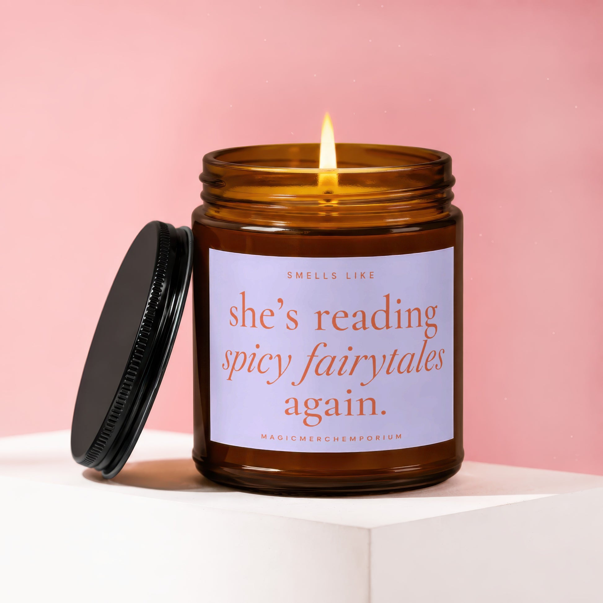 Amber jar candle with lit flame, reading "she's reading spicy fairytales again."
