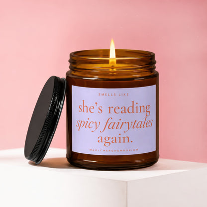 Amber jar candle with lit flame, reading "she's reading spicy fairytales again."