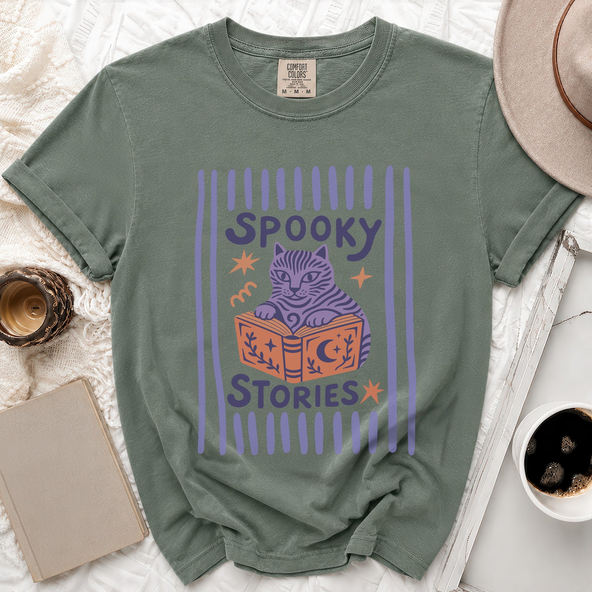 Green t-shirt graphic with purple striped background, cat reading "Spooky Stories."