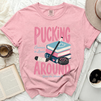 Pink t-shirt with "Pucking Around Enemies to Lovers" text and hockey stick.