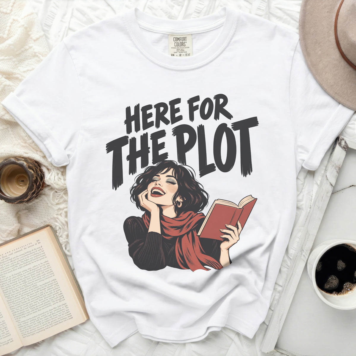 White t-shirt with "HERE FOR THE PLOT" text and illustration of woman reading.