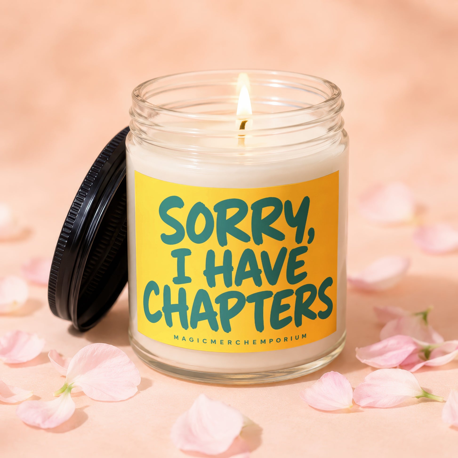 Glass candle with lit wick on yellow label reading "SORRY, I HAVE CHAPTERS".