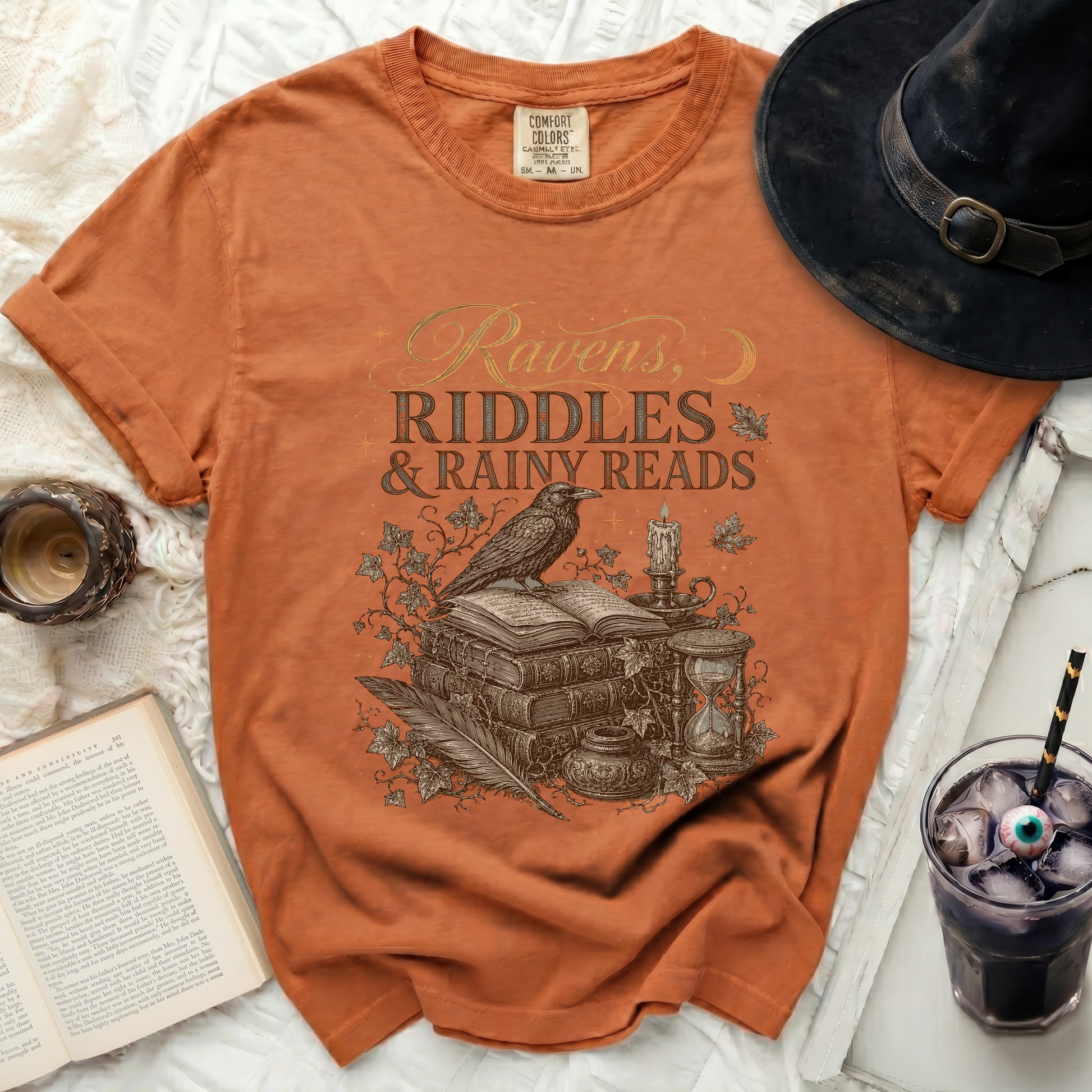 Orange comfort colors t-shirt with "Ravens, Riddles & Rainy Reads" graphic.