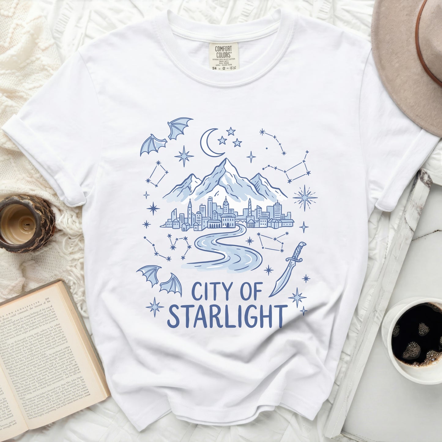 White t-shirt with blue graphic of a city, mountains, stars, and text "City of Starlight".