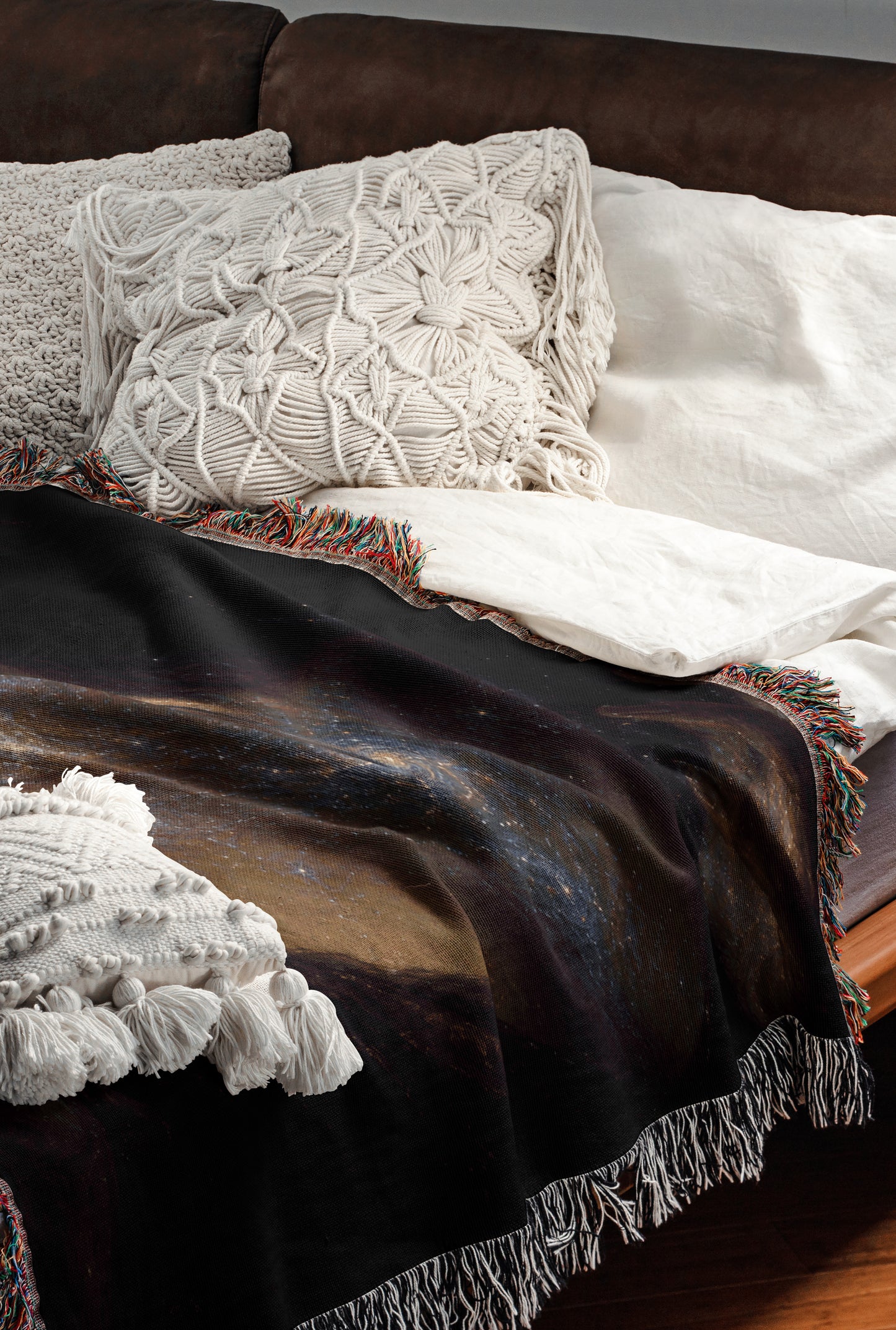 a cozy and inviting bedroom scene, featuring a comfortable bed with a black blanket and white pillows, as well as a colorful throw blanket with fringe.