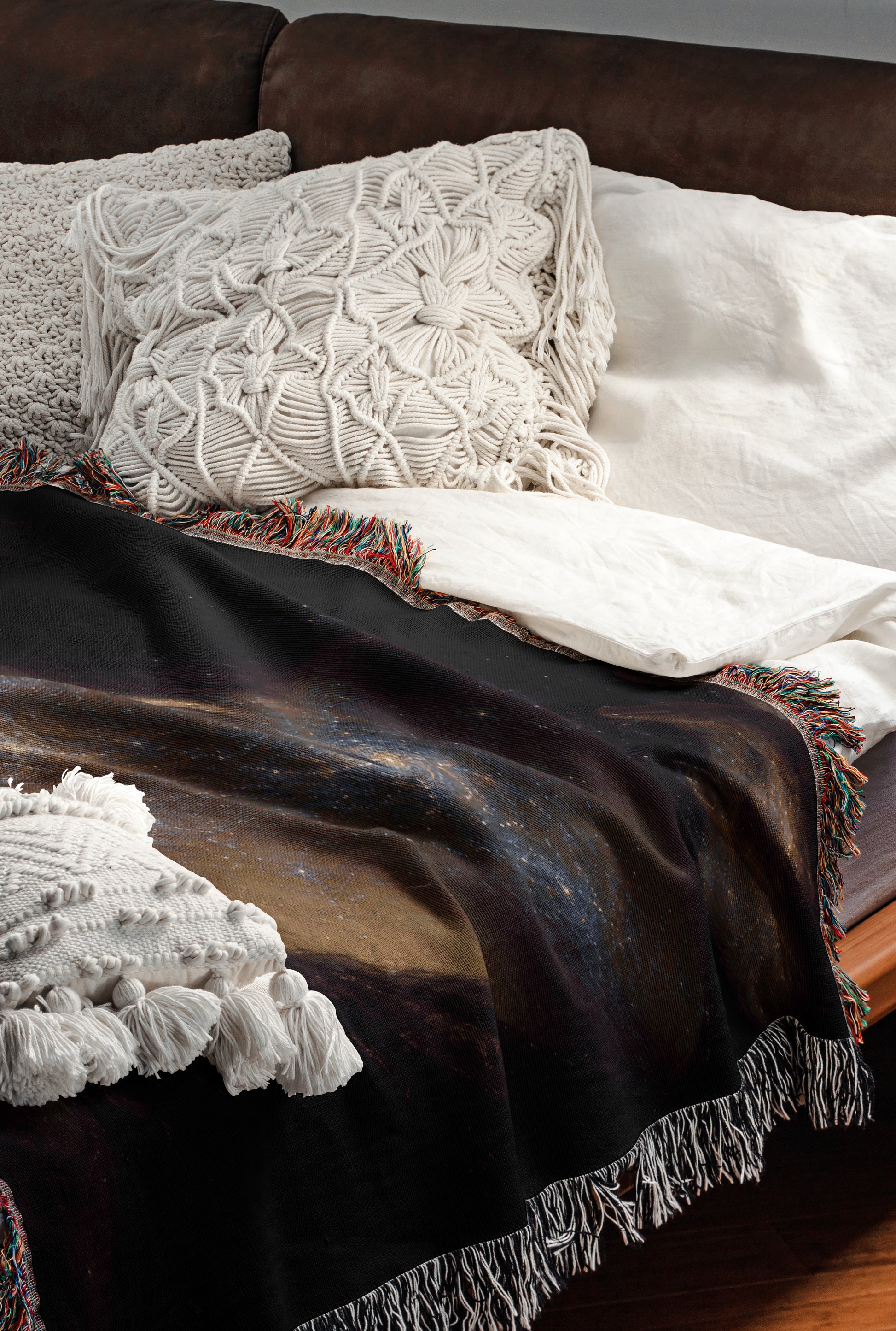 a cozy and inviting bedroom scene, featuring a comfortable bed with a black blanket and white pillows, as well as a colorful throw blanket with fringe.