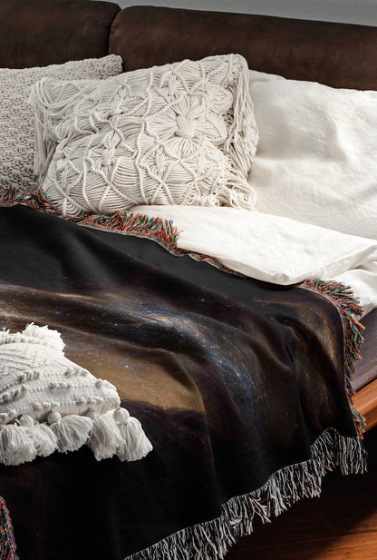 a cozy and inviting bedroom scene, featuring a comfortable bed with a black blanket and white pillows, as well as a colorful throw blanket with fringe.