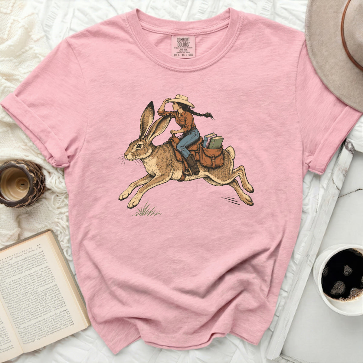 Pink t-shirt with illustration of woman riding a rabbit with books.