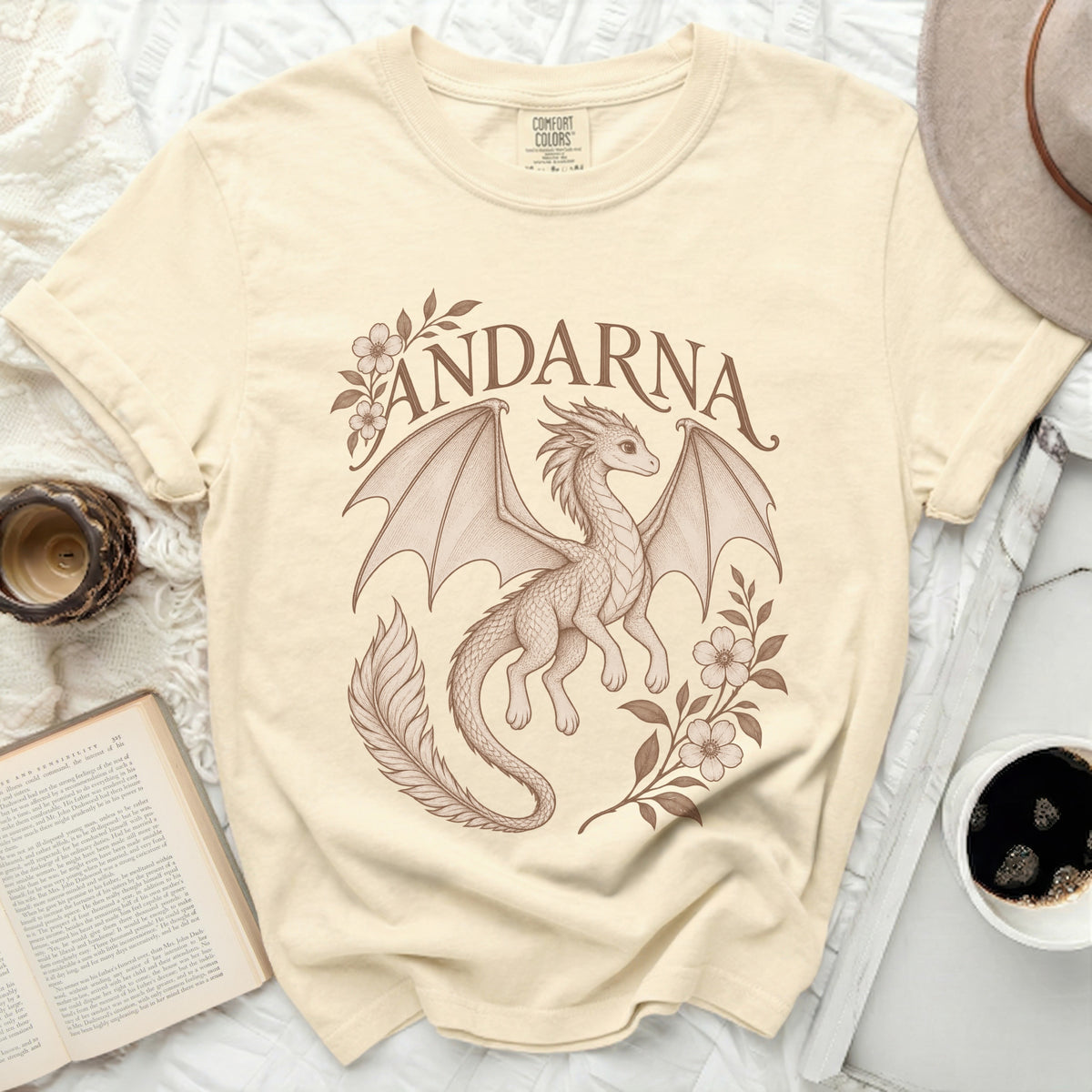 Beige t-shirt featuring a brown vintage-style drawing of a winged dragon, flowers, and the word ANDARNA.