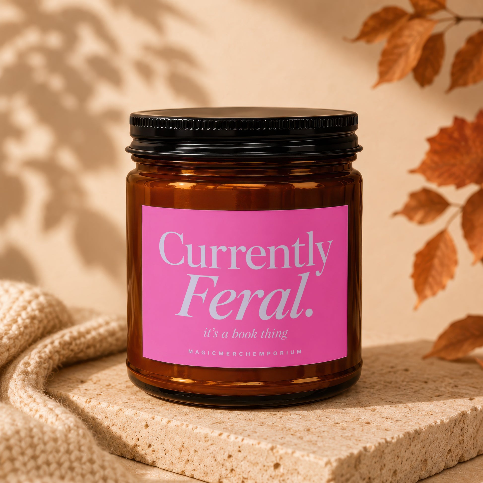 Amber jar candle with pink label reading "Currently Feral. it's a book thing".