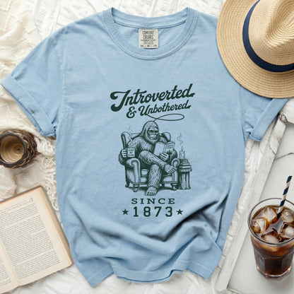 Bigfoot reading a book and holding a mug on a blue t-shirt.