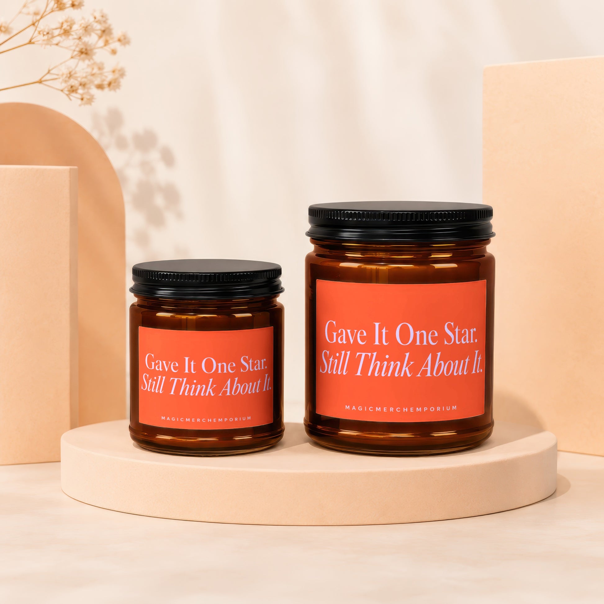 Two amber glass candles with black lids and orange labels reading "Gave It One Star. Still Think About It."