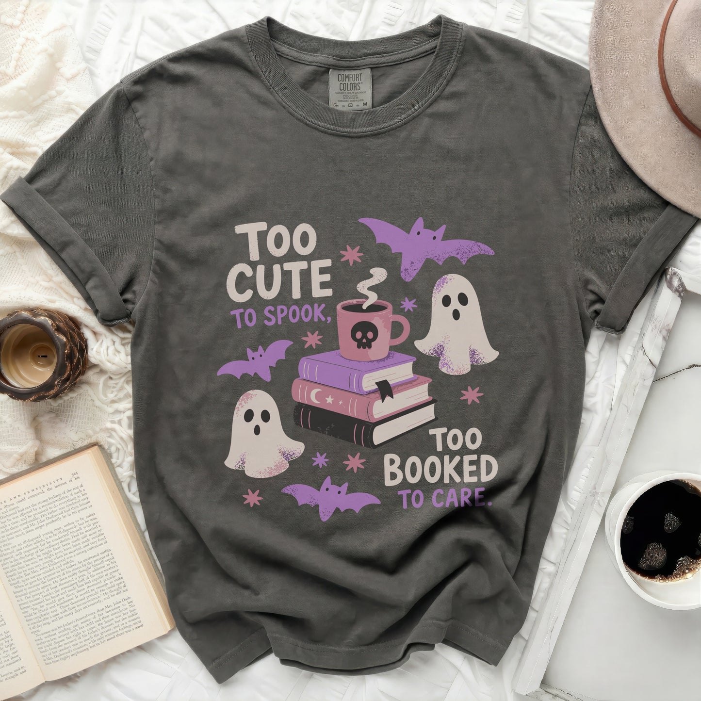 Grey t-shirt graphic with ghosts, books, bats, and text "Too cute to spook, too booked to care."