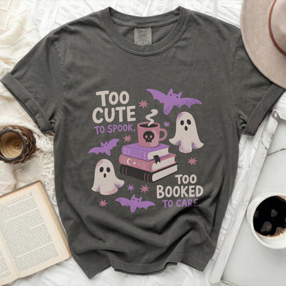 Grey t-shirt graphic with ghosts, books, bats, and text "Too cute to spook, too booked to care."