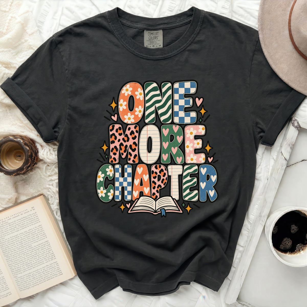 Graphic tee with "ONE MORE CHAPTER" text in colorful, patterned letters.