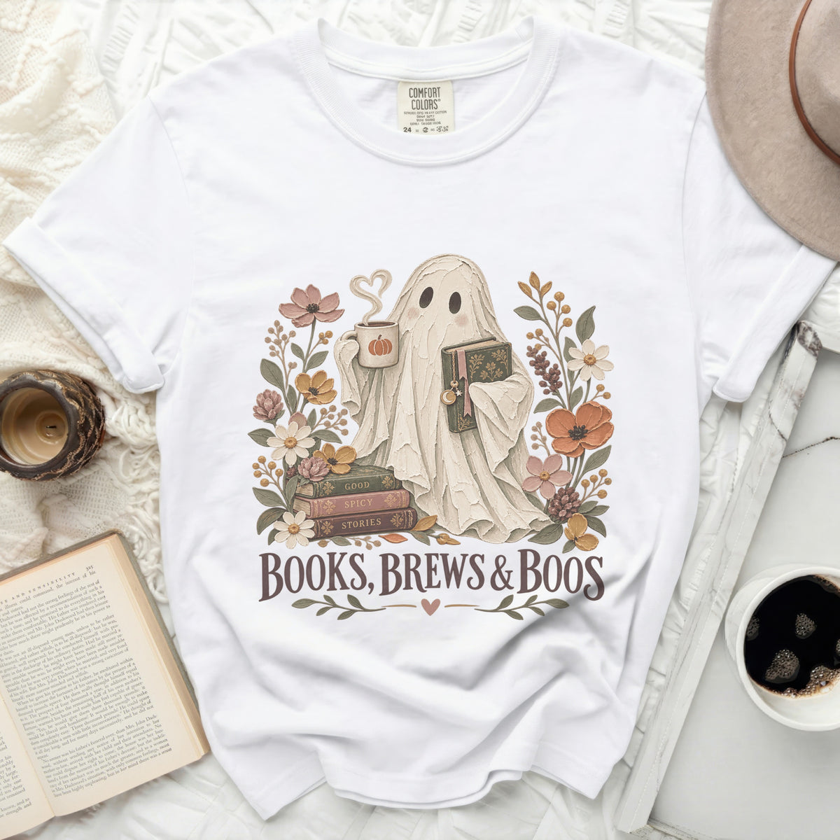 White t-shirt with a ghost holding coffee and book, surrounded by flowers. Text reads "Books, Brews & Boos".
