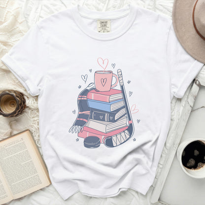 White t-shirt with stacked books, hot cocoa, and hockey stick graphic.