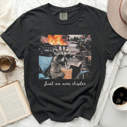 T-shirt with raccoon in a chair, coffee, and fire, reads "Just one more chapter".