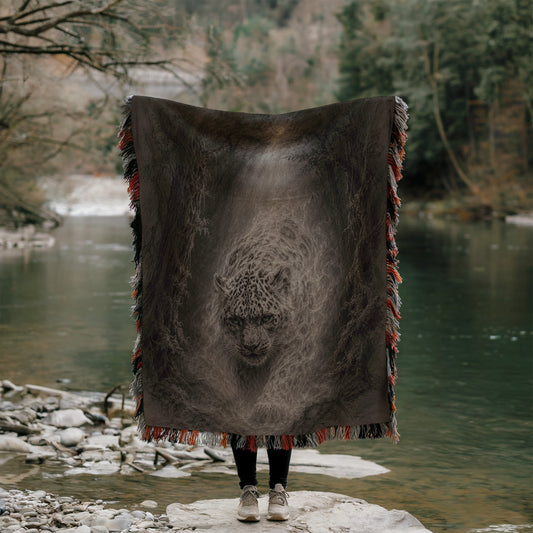 A person stands on a rock, holding a large blanket with a picture of a leopard on it, in front of a body of water surrounded by trees.