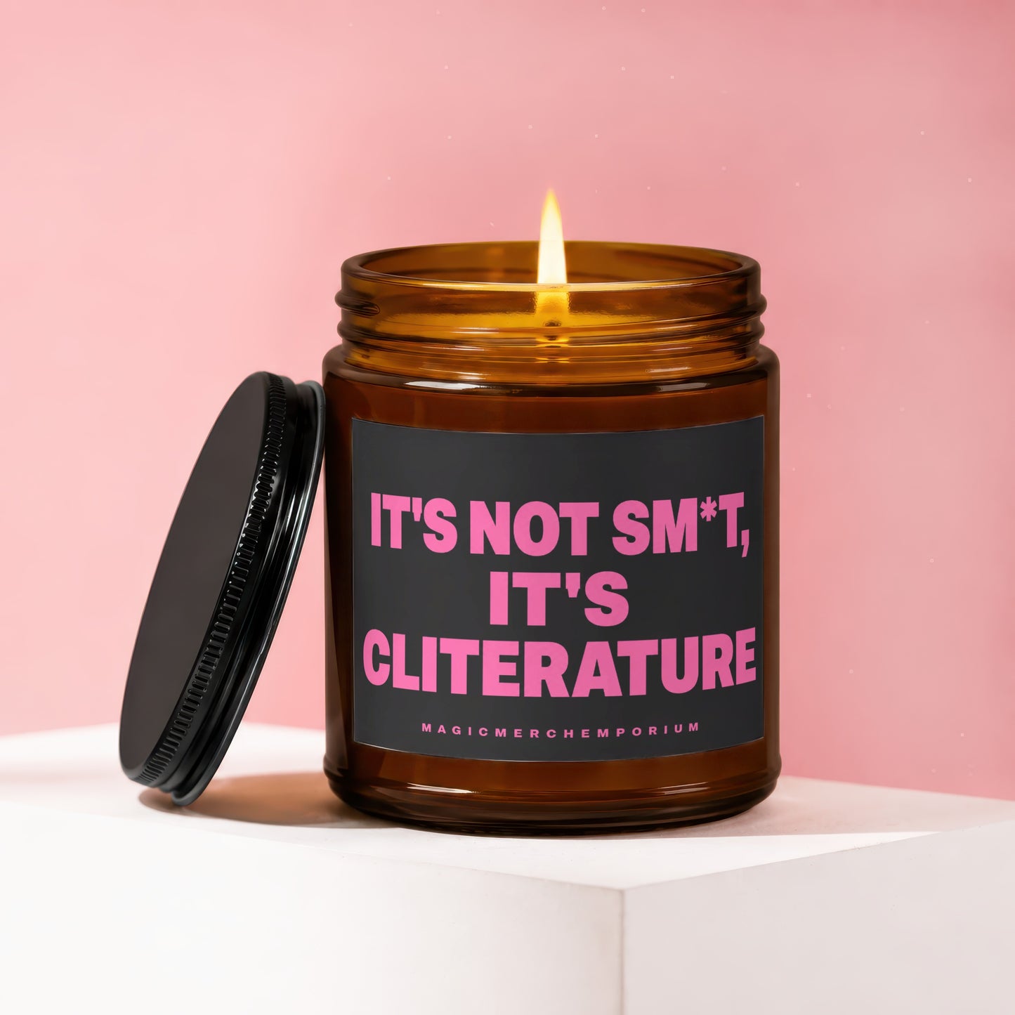 Amber candle with lit flame, black lid, and black label reading "IT'S NOT SM*T, IT'S CLITERATURE".