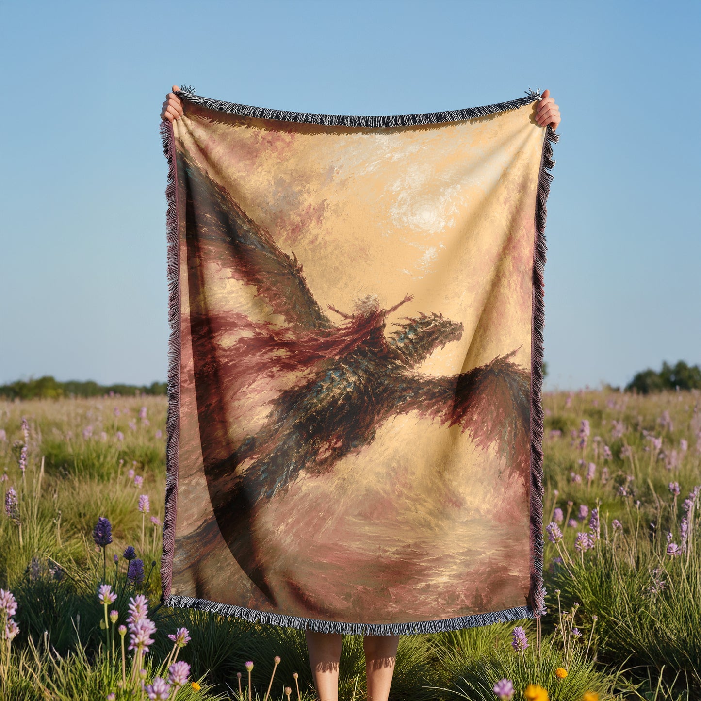 A person is holding up a large, colorful blanket with a dragon design in a field of purple flowers.