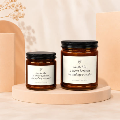 Two amber glass candles with black lids, each labeled "smells like a secret between me and my e-reader".
