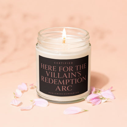 Jar candle with lit wick, "Here for the Villain's Redemption Arc" text, pink petals.