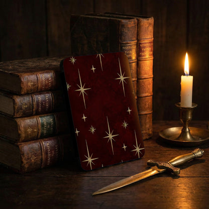 Red card with star pattern, antique books, candle, and dagger on wooden surface.