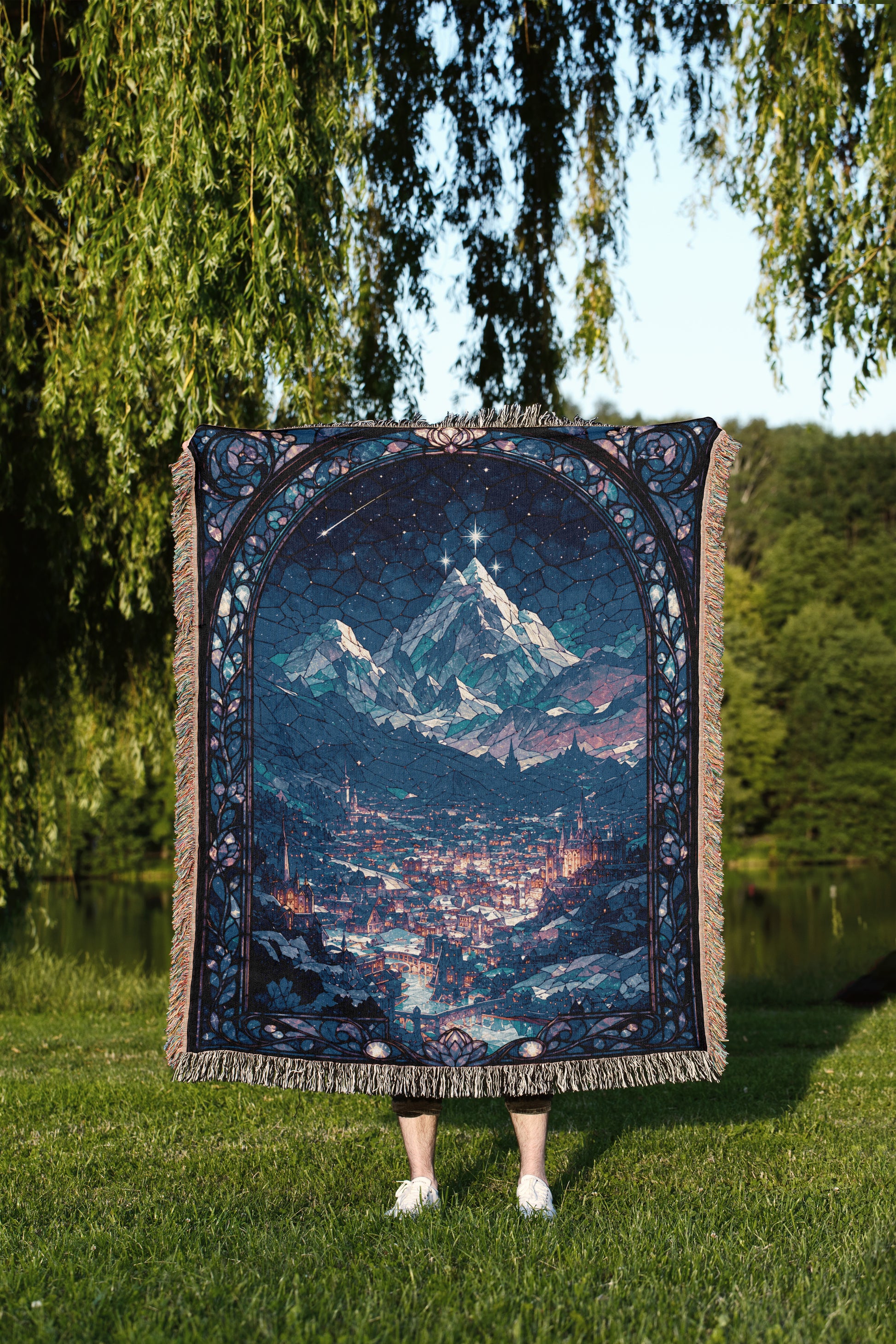 A person is standing in a grassy area, holding a large, intricately designed tapestry or blanket that features a night sky scene with mountains and a castle.