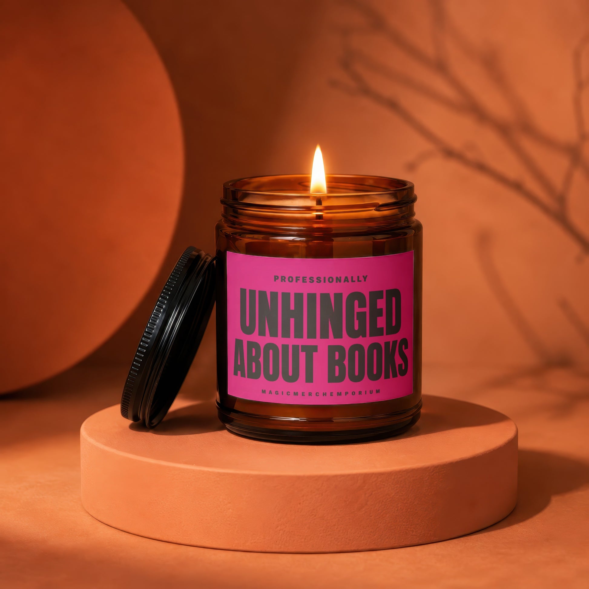 Amber glass candle with pink label reading "Professionally Unhinged About Books".
