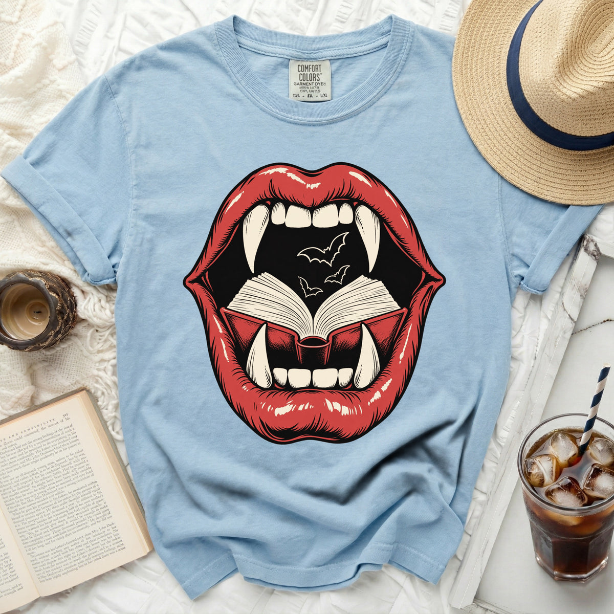 Light blue t-shirt with graphic of red lips, fangs, an open book, and bats.