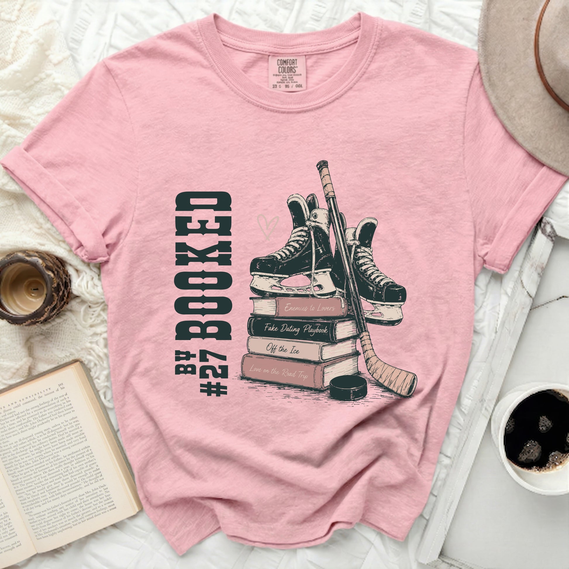 Pink t-shirt with stack of books, ice skates, hockey stick, and text.