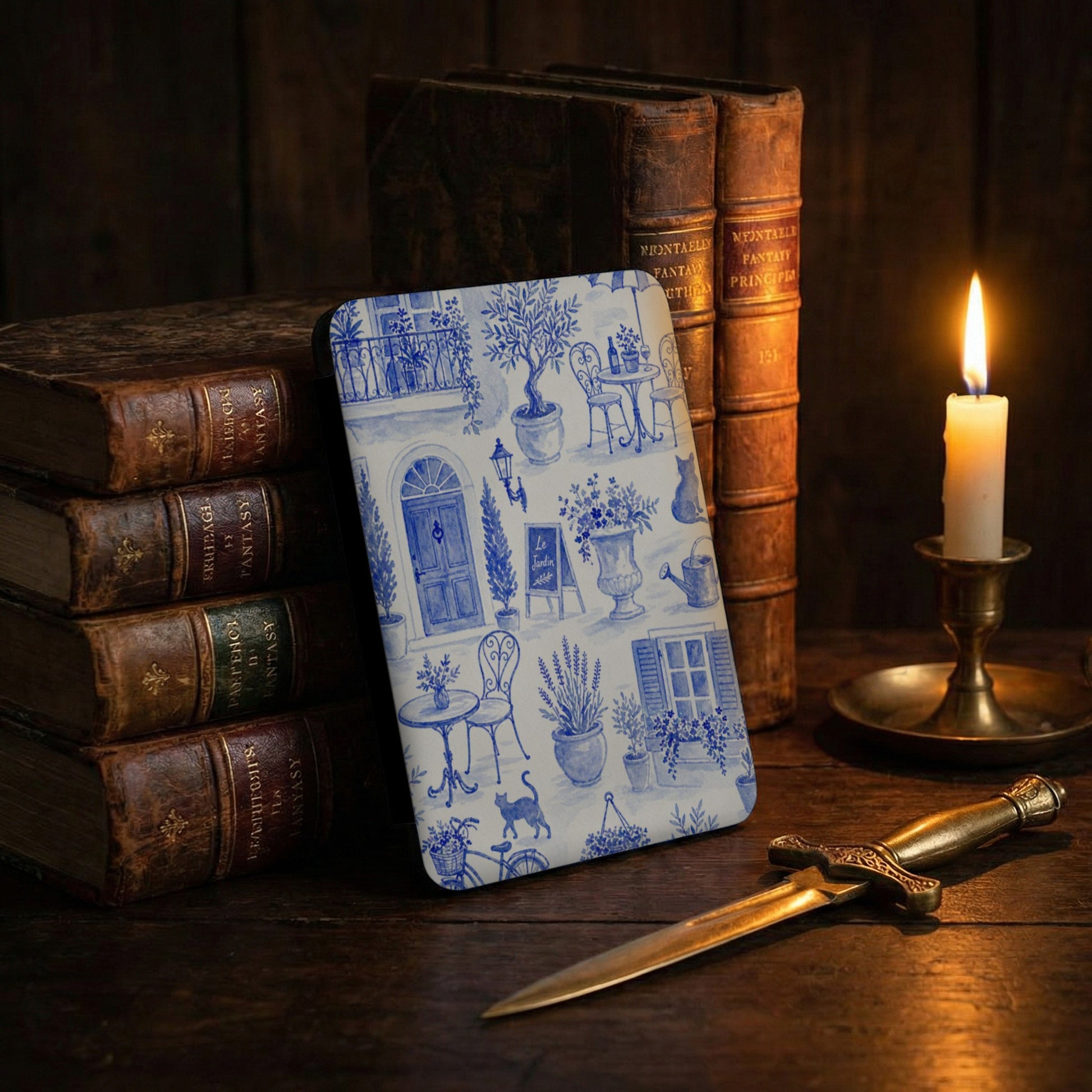 Blue and white toile pattern with French courtyard scene on a case, near old books and candle.