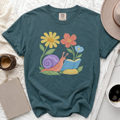 Teal t-shirt with a graphic of a snail reading a book among flowers.
