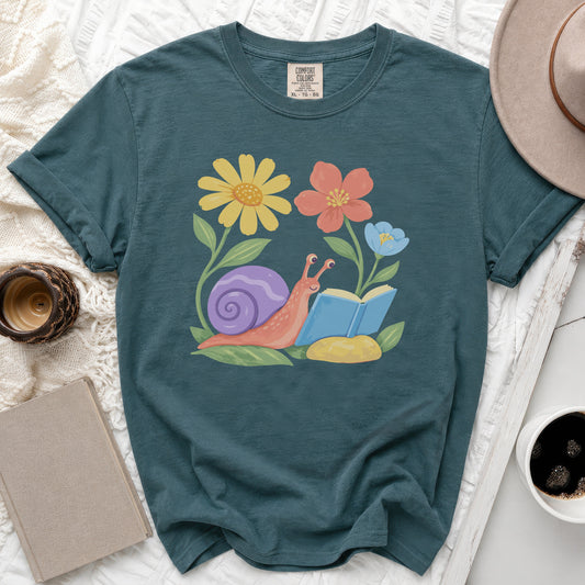 Teal t-shirt with a graphic of a snail reading a book among flowers.