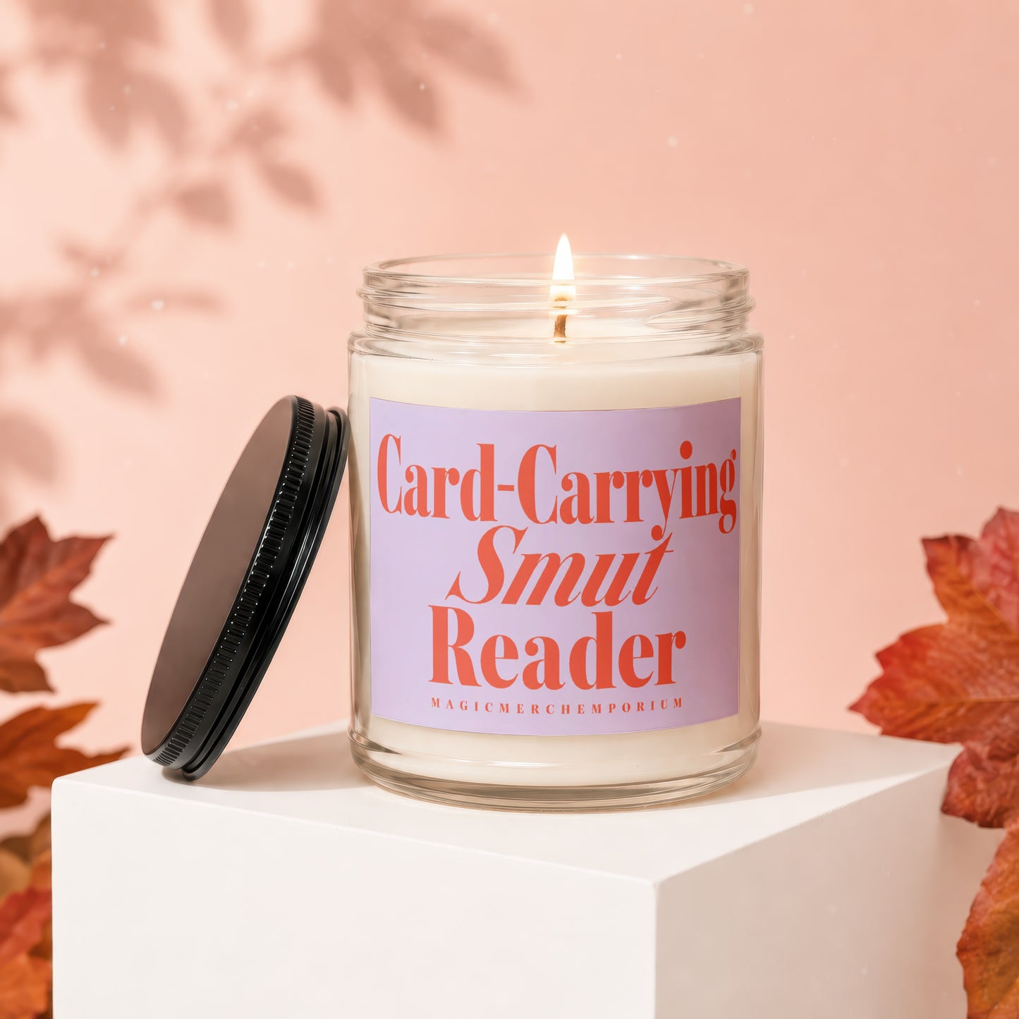 Lit candle in jar with "Card-Carrying Smut Reader" label, on white cube.