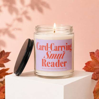 Lit candle in jar with "Card-Carrying Smut Reader" label, on white cube.